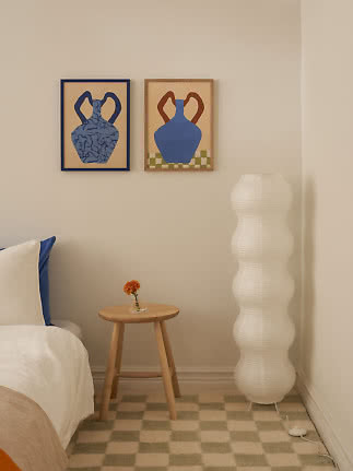 Coin chambre cosy avec deux affiches de vases, petite table en bois et grande lampe sur pied blanche