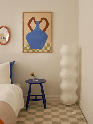 Coin chambre cosy avec tabouret bleu, grand lampadaire blanc et affiche encadrée de vase au mur