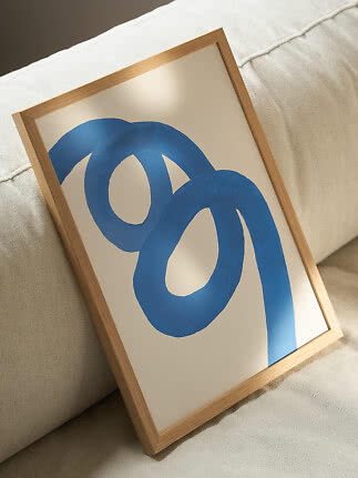 Framed abstract print with blue looping shapes, leaning against a beige sofa