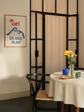 Spisehjørne med rundt bord, blomster i vase, krus og fransk plakat på væggen