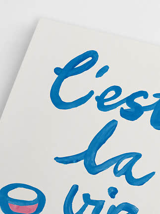 Close-up of white poster with blue hand-painted lettering and small pink detail at the bottom