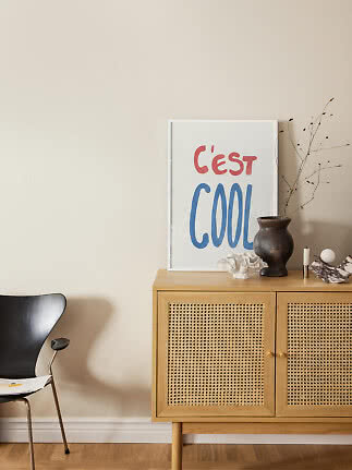 "C'est Cool"-Poster auf Holzschrank mit Vase und Deko in einem hellen Raum