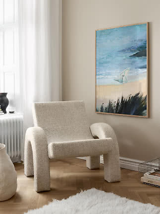 Cream bouclé armchair beside a framed beach painting in a bright corner