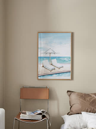 Stampa da spiaggia incorniciata con due lettini e ombrellone vista mare su parete beige
