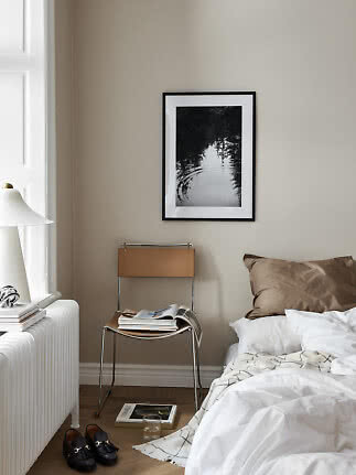 Hyggeligt soveværelse med uopredt seng, lænestol, bordlampe og sort-hvidt billede på væggen