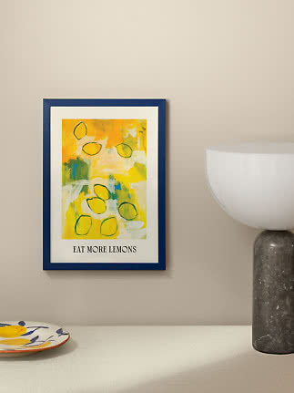 Ingelijste citroenposter met blauwe lijst en tekst "EAT MORE LEMONS" aan beige muur