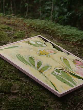 Indrammet abstrakt blomstermaleri med grønne og rosa toner, placeret på mosbund i skov