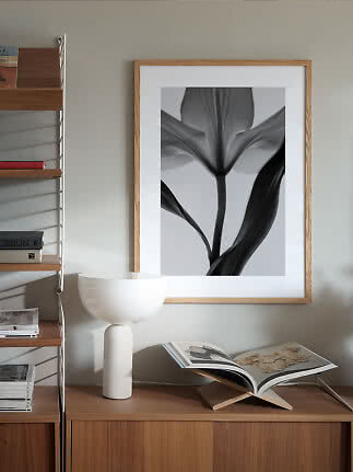 Indrammet sort-hvid blomsterplakat over træskænk med hvid bordlampe og åben bog