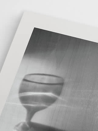 Schwarz-weißer Kunstdruck mit unscharfem Cocktailglas vor grauem Holz-Hintergrund