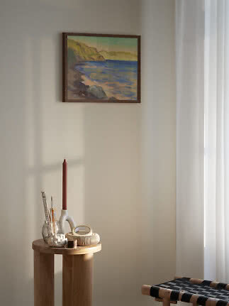 Pintura costera enmarcada sobre una mesa redonda de madera con candelero y pequeños adornos