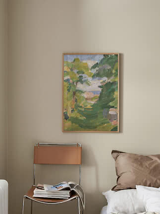Cuadro abstracto de paisaje enmarcado en pared beige sobre una silla junto a la cama