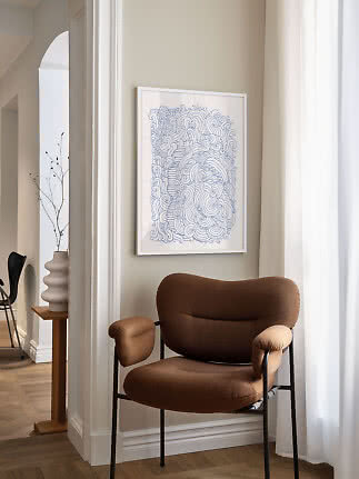 Framed abstract blue line drawing above a brown lounge chair by a bright window