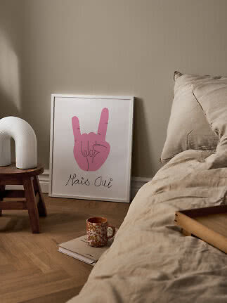 Indrammet plakat med pink håndtegn lænet op ad væggen ved seng i beige soveværelse