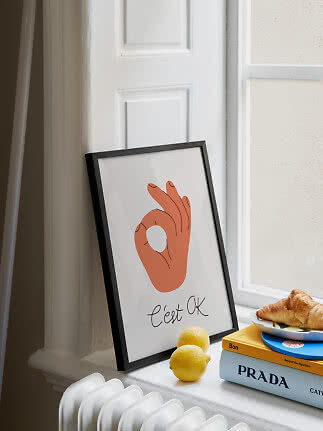 Indrammet plakat med håndtegn ved et vindue, med citroner, bøger og croissant på karmen