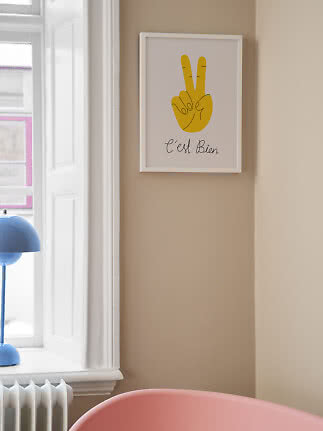 Indrammet plakat med gul fredshånd og teksten "C'est Bien" på beige væg