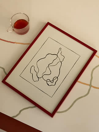 Abstract line drawing in a red frame on a table beside a glass cup of tea