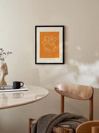 Gerahmter abstrakter orangefarbener Kunstdruck an der Wand über Tisch und Holzstuhl