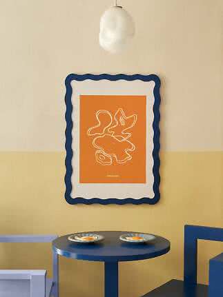Orange abstraktes Poster im welligen blauen Rahmen über rundem blauem Tisch mit zwei Tellern