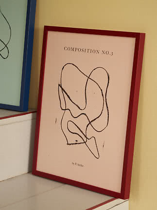 Abstrakt poster med svarta linjer i röd ram, lutad mot gul vägg i en trappa
