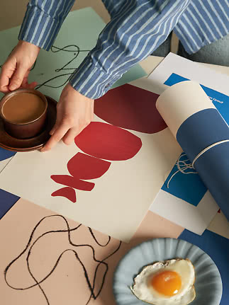 Handen in blauw gestreept overhemd verplaatsen een koffiekop boven kleurrijke prints en een bord met ei