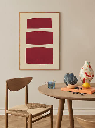 Abstracte wandkunst met drie rode vormen in houten lijst boven tafel en stoel