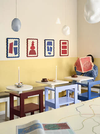 Kleurrijk café-interieur met abstracte wandkunst, hanglampen, kleine tafels, kaarsen en een persoon met boek