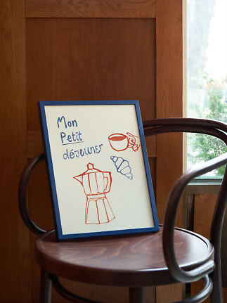 Indrammet plakat med fransk tekst og tegninger af kaffekop, croissant og mokakande på træstol