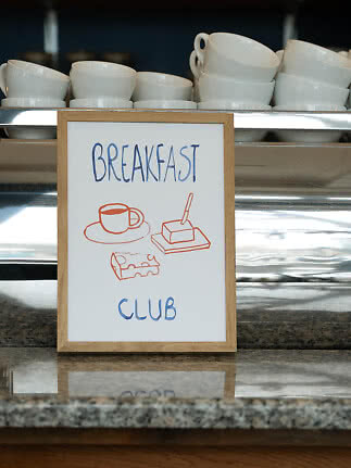 Cartello "Breakfast Club" davanti a tazze bianche impilate su un buffet.