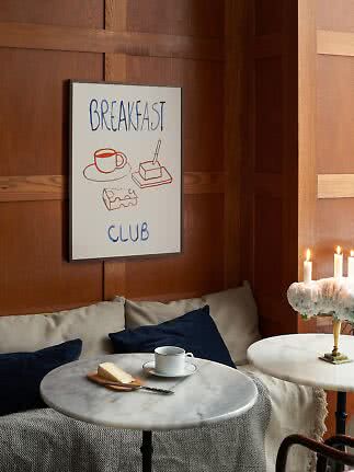 Poster incorniciato "Breakfast Club" su parete in legno sopra tavolino con tazza e burro.