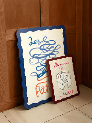 Zwei dekorative Schilder mit gewelltem Rand, ein großes mit blauer Schrift und ein kleines mit Kuchenzeichnung.
