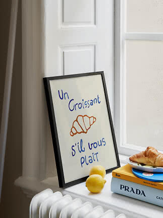 Indrammet croissant-plakat på en vindueskarm med citroner, bøger og en croissant på en tallerken