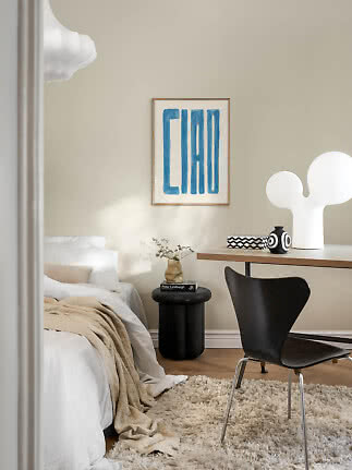 Lyst soveværelse med hvid seng, skrivebord, sort stol og hvid bordlampe