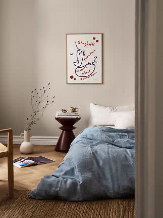 Chambre avec couette bleue, table d'appoint foncée et affiche encadrée sur mur beige