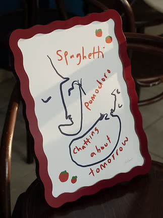 Panneau décoratif à bord ondulé rouge, dessin de visages et texte spaghetti pomodoro sur une chaise