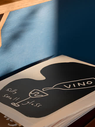 Nærbillede af kunstbog med sort-hvid omslag og teksten "VINO" på et bord ved blå væg
