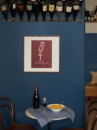 Pequeña mesa de café con botella de vino, copa de vino tinto y cuenco de pasta