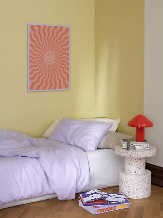 Lit avec linge de lit lilas clair, mur jaune, lampe rouge et affiche colorée au-dessus