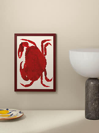Framed poster of a red crab on a light wall beside a table lamp