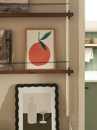 Inramad apelsinbild på mörk trähylla med magasin och konst