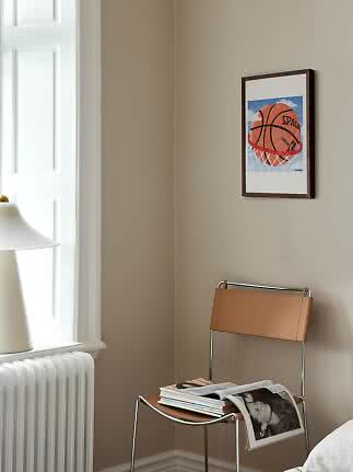 Framed basketball print on a beige wall above a chair with magazines in a bright room corner