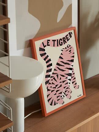 Gerahmtes Poster mit rosa Tiger und dem Schriftzug „Le Tigre“ auf einem Holzregal