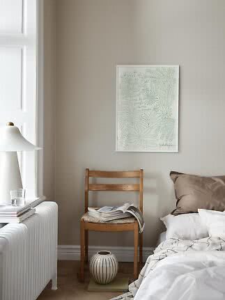 Framed botanical print with green line drawings above a wooden chair beside a bed