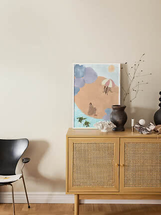 Framed abstract beach print on an oak sideboard with vase, coral and candle against a beige wall