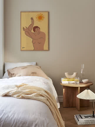 Bedroom with bed, round nightstand, and poster of a woman under a sun on a beige wall