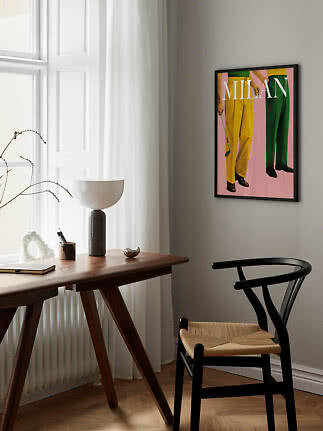 Framed Milano poster on gray wall above wooden desk and black chair by a window