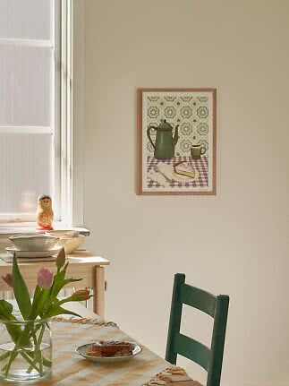Zonnige eethoek met groene stoel, tulpen op tafel en ingelijste stillevenprint aan de muur