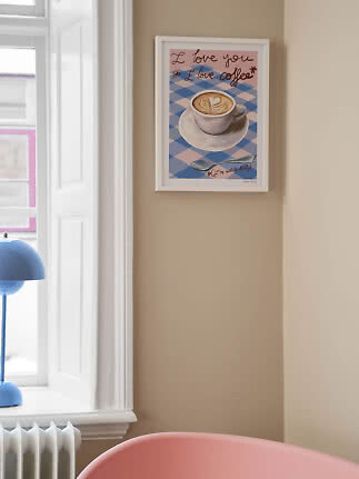 Inramad kaffeposter med latte art och text på beige vägg bredvid ett fönster
