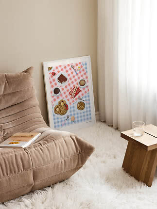 Ingelijste keukenposter met koffie en gebak, leunend tegen de muur bij fauteuil en houten tafeltje