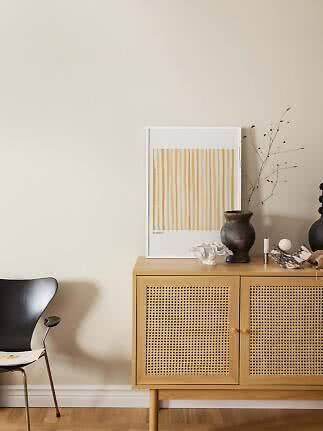 Lyst træskab med fletlåger, vase, koral og gulstribet plakat i minimalistisk stue