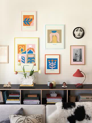 Living room wall with colorful framed art above a black sideboard with vase, tulips and red lamp